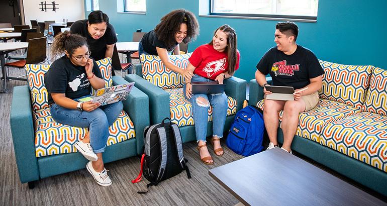 Students sitting on couches with computers, talking.